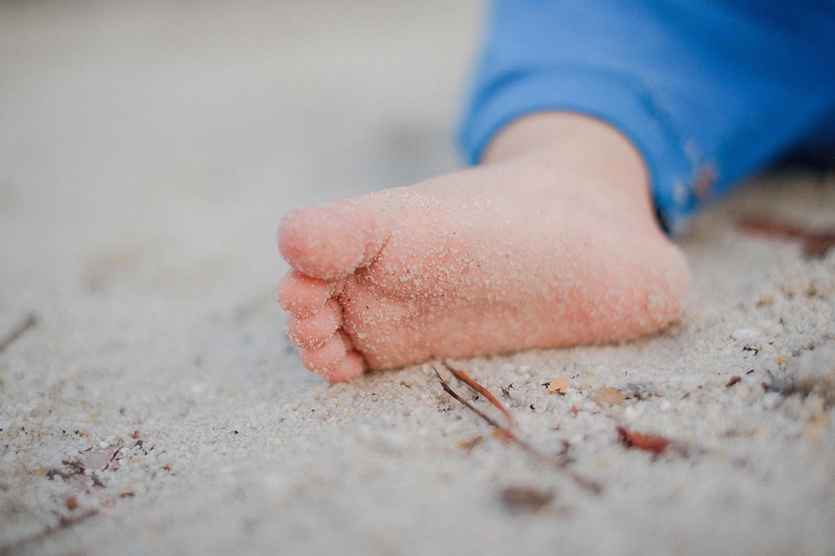 Photo of a baby foot on a beach, with a little of sand on sole of the foot