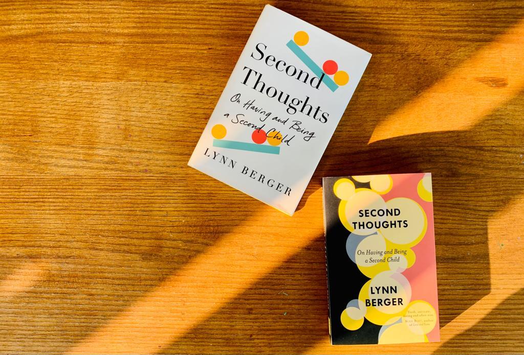 A picture with a wooden surface with the two editions of the book Second Thoughts displayed on it.