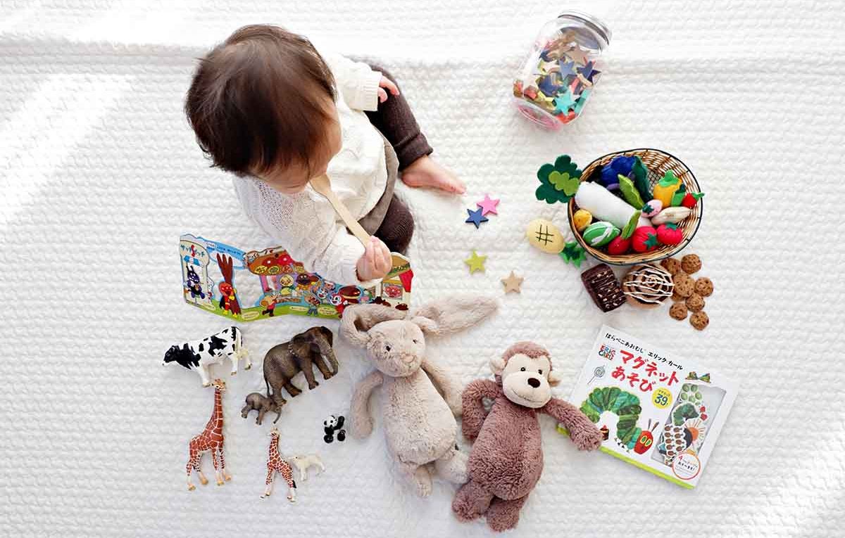 Child sitting on white cloth surrounded by toys.