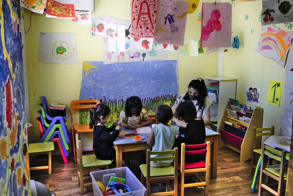 Children sitting around a table with a teacher doing crafts.