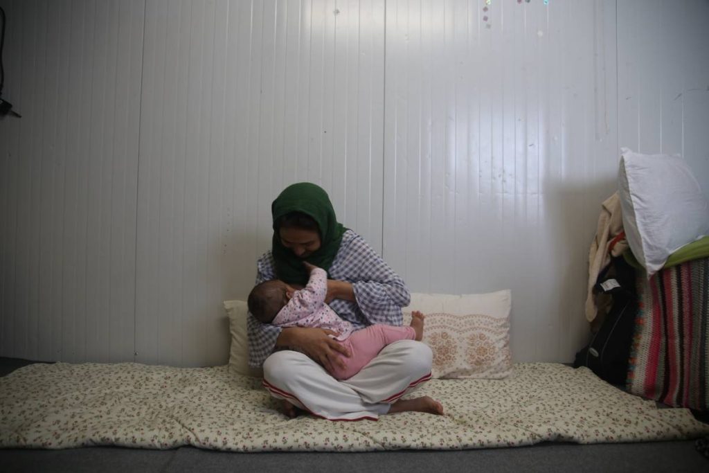A woman in a headscarf is breastfeeding her baby sitting on the ground